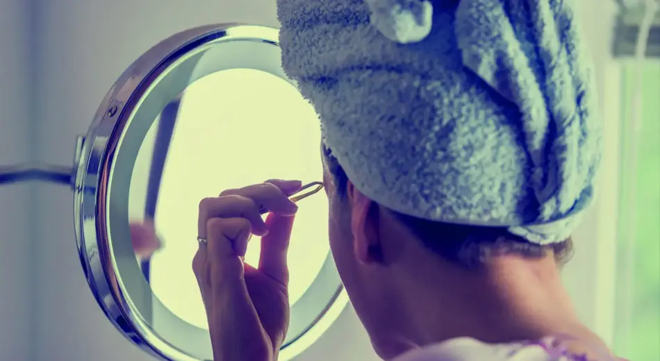 Frau mit Handtuch Turban beim Augenbrauen zupfen