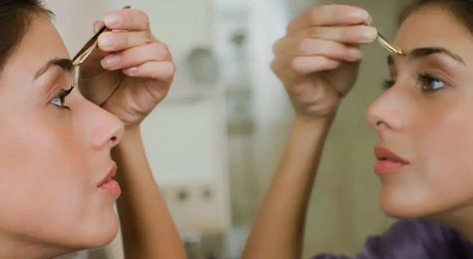 Frau vorm Spiegel beim Augenbrauen zupfen