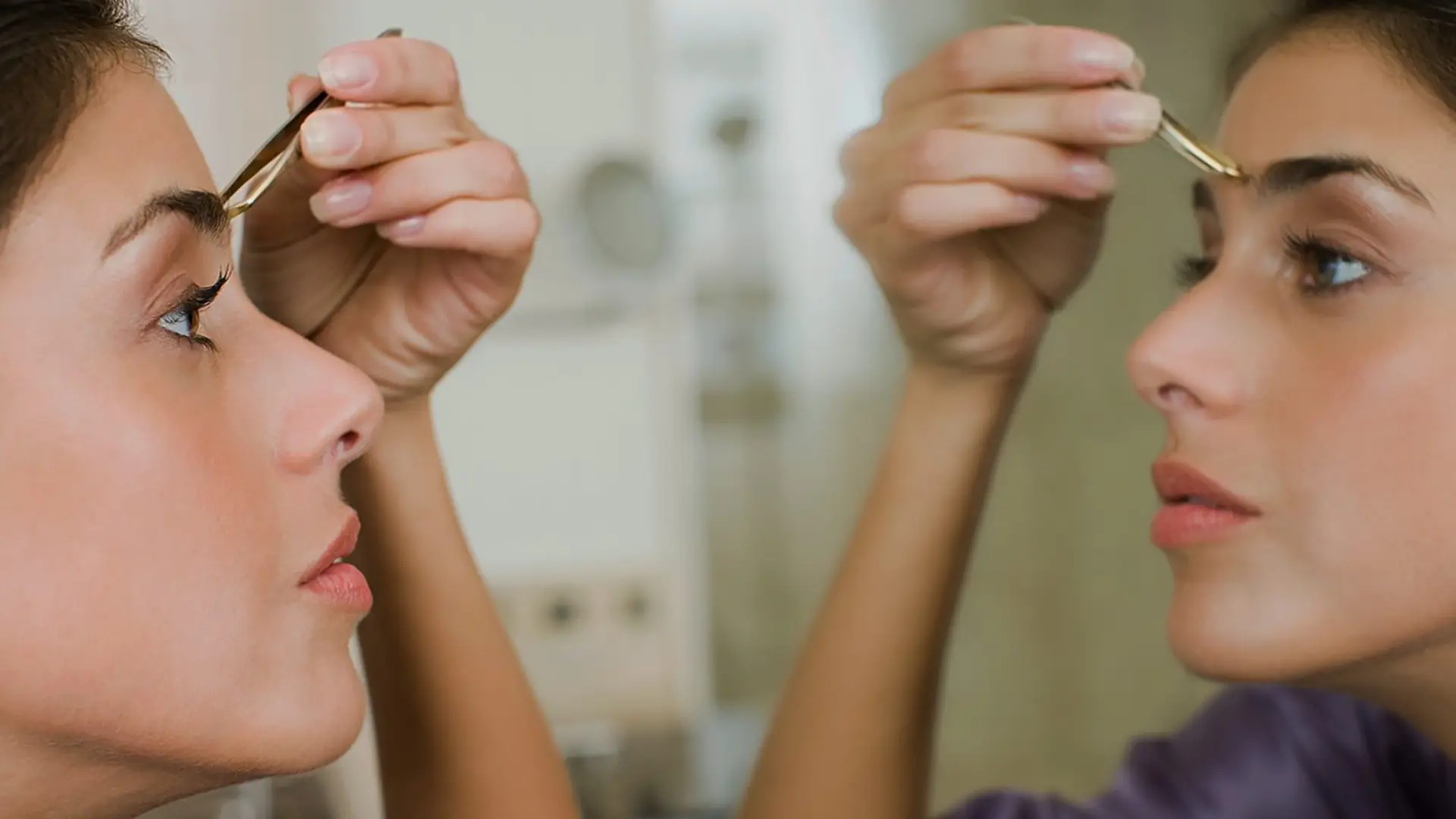 Frau vorm Spiegel beim Augenbrauen zupfen