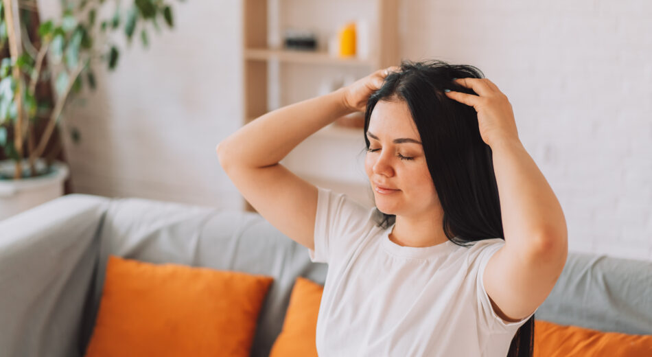Eine Frau mit schwarzem Haar massiert sich selbst die Kopfhaut.
