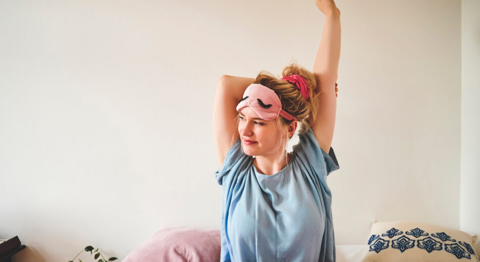 Ausschnitt einer jungen Frau, die morgens nach dem Aufwachen im Bett sitzt und sich streckt.