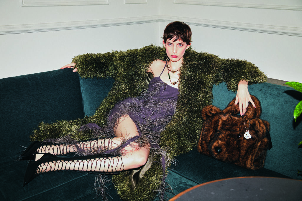 Frau in grünem flauschigen Mantel auf einer Couch posierend