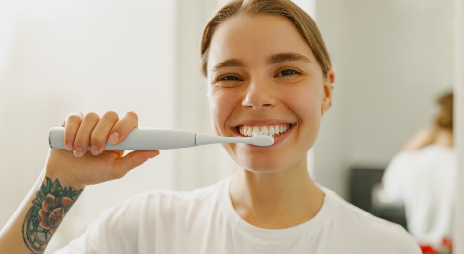 Eine junge Frau putzt sich vergnügt die Zähne und präsentiert stolz ihre Zähne.