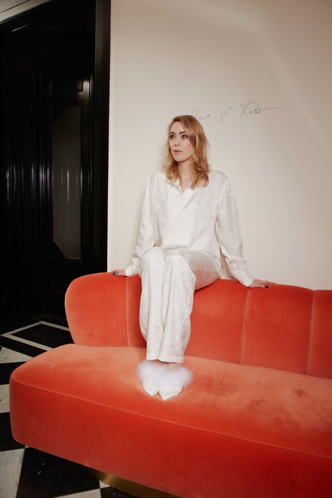 Laura Sänger alias La Katz in weissem Outfit auf oranger Couch