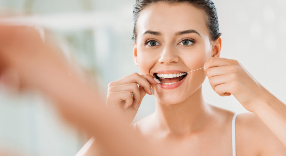 Selektiver Fokus auf ein schönes, lächelndes Mädchen, das im Badezimmer Zahnseide benutzt.