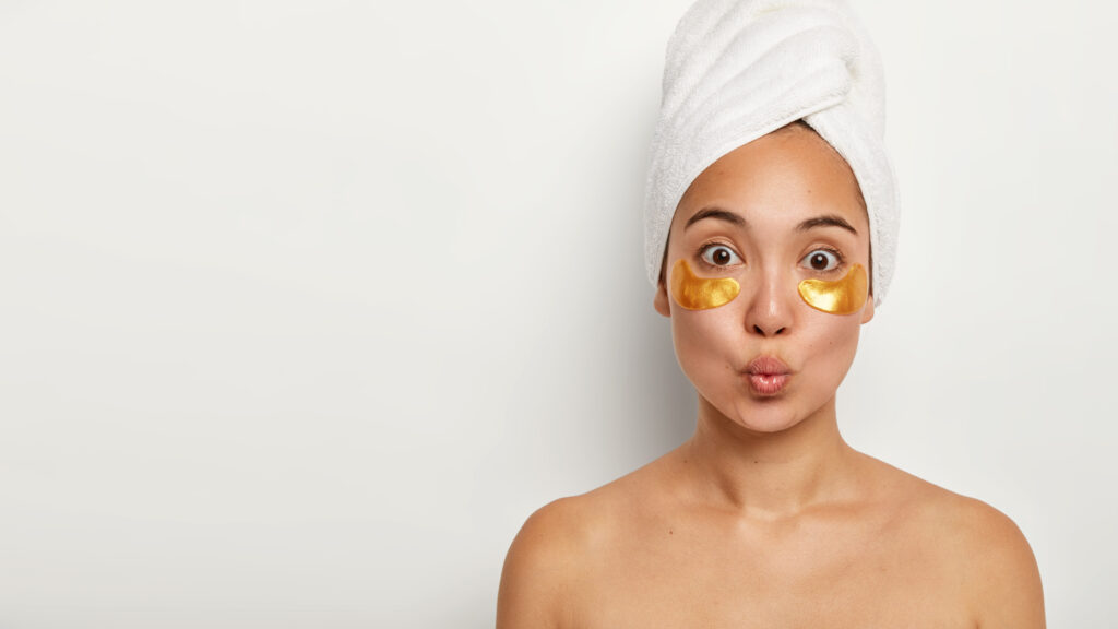 Frau macht Spa-Behandlung zu Hause, hat eine frische, gesunde Haut, hält ihre Lippen geschürzt, verwendet Augenpads gegen Augenringe