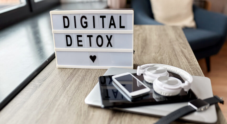 Schriftzug Digital Detox auf Leuchtkasten, digitale Geräte gestapelt daneben