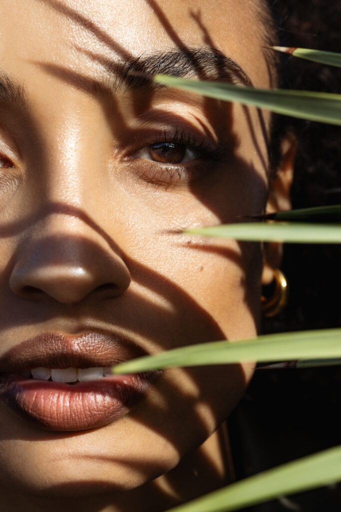 maxima Sonnenschutz Editorial Shooting, Nahaufnahme Gesicht, halb im Schatten einer Pflanze