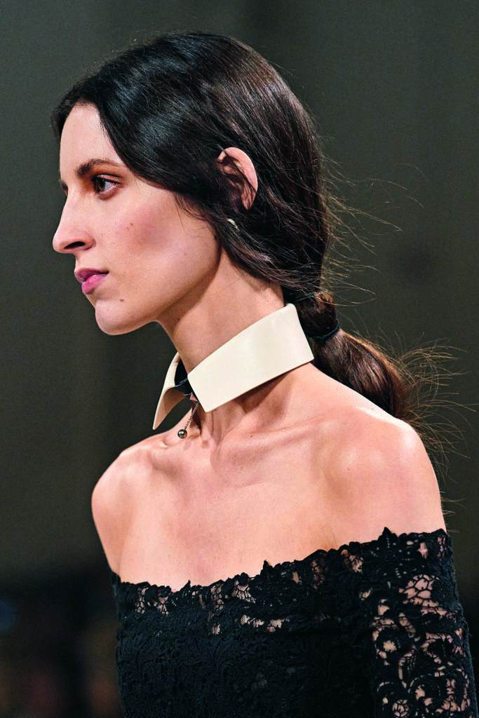 Frau am Laufsteg, in schwarzem Spitzenoberteil und weisser Manschette um den Hals, dunkle lange Haare zu einem out-of-bed-Pferdeschwanz gebunden, Kollektion Fendi